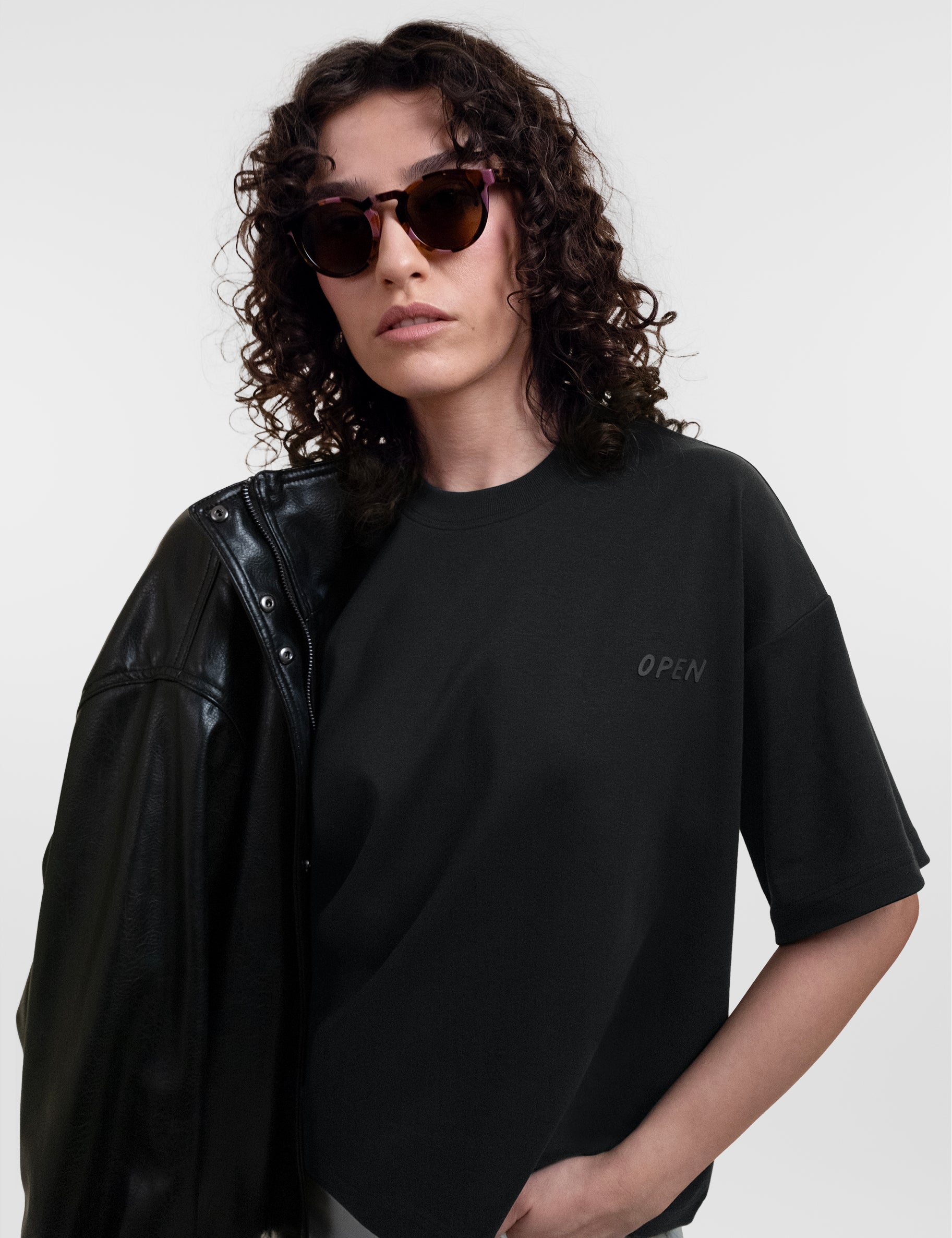 Open Row Women's Open Heart Tee in black, front editorial view paired with a leather jacket and sunglasses.