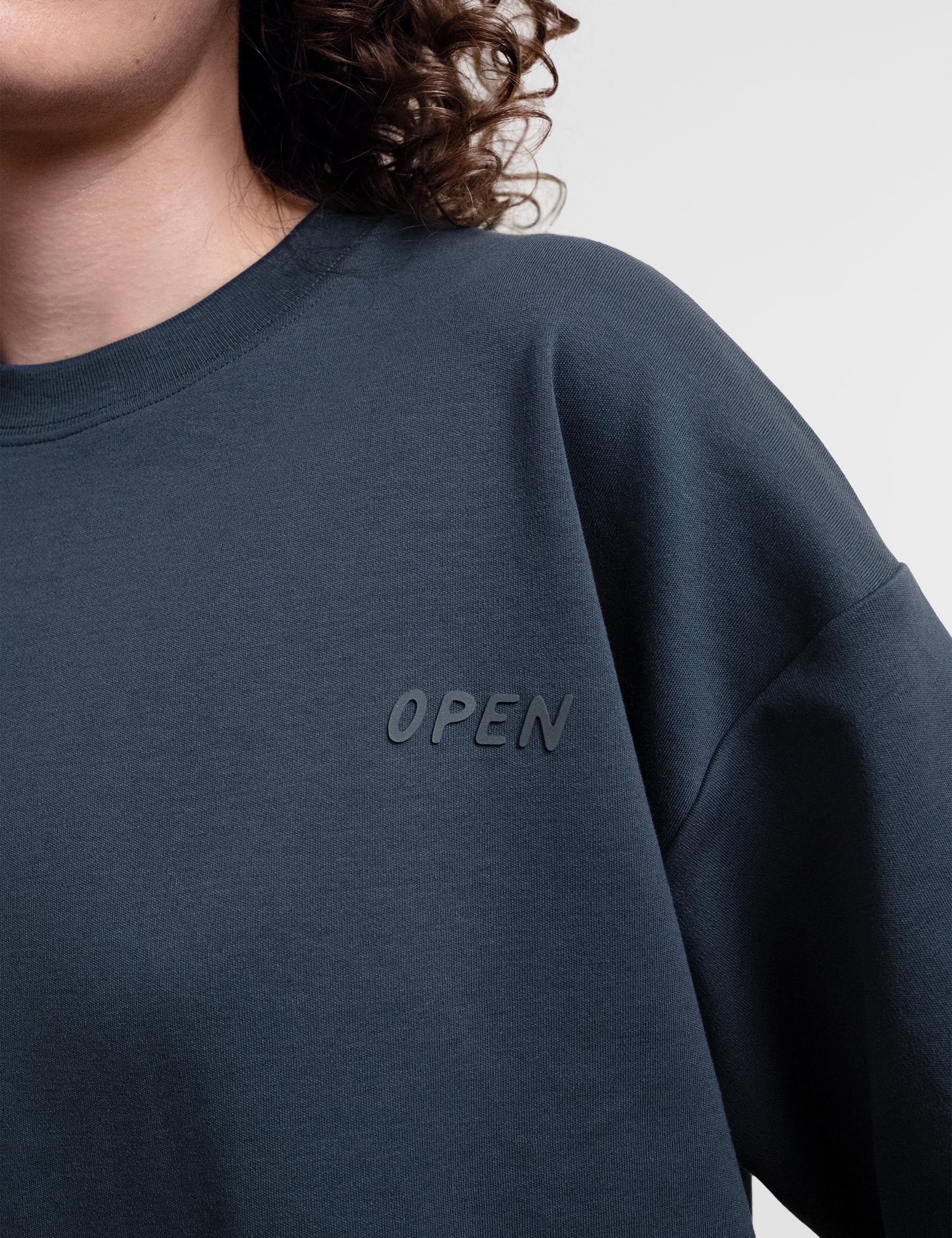 Open Row Women's Open Heart Tee in navy blue, closeup view, embossed logo detail.