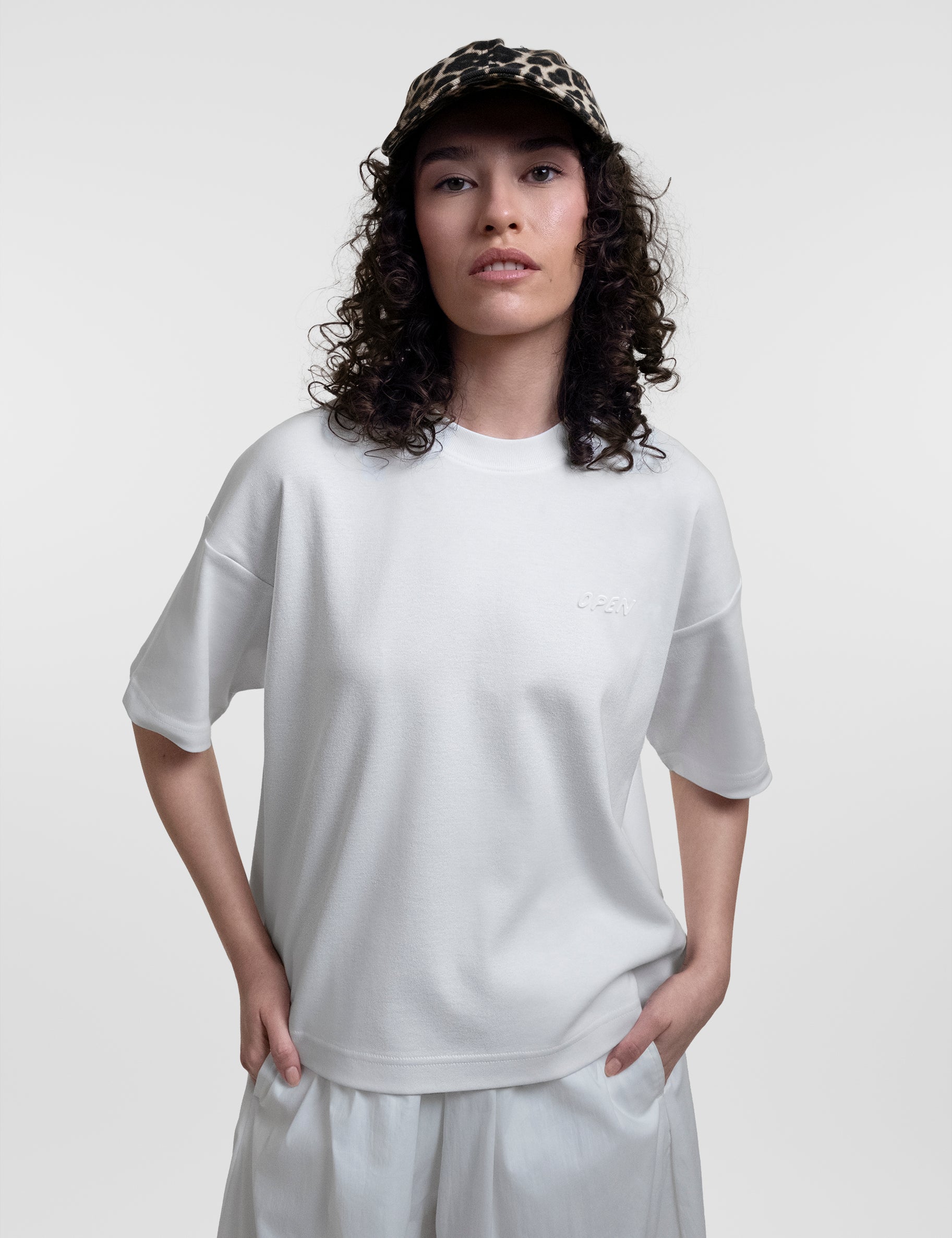 Open Row Women's Open Heart Tee in white, front view paired with a baseball cap.