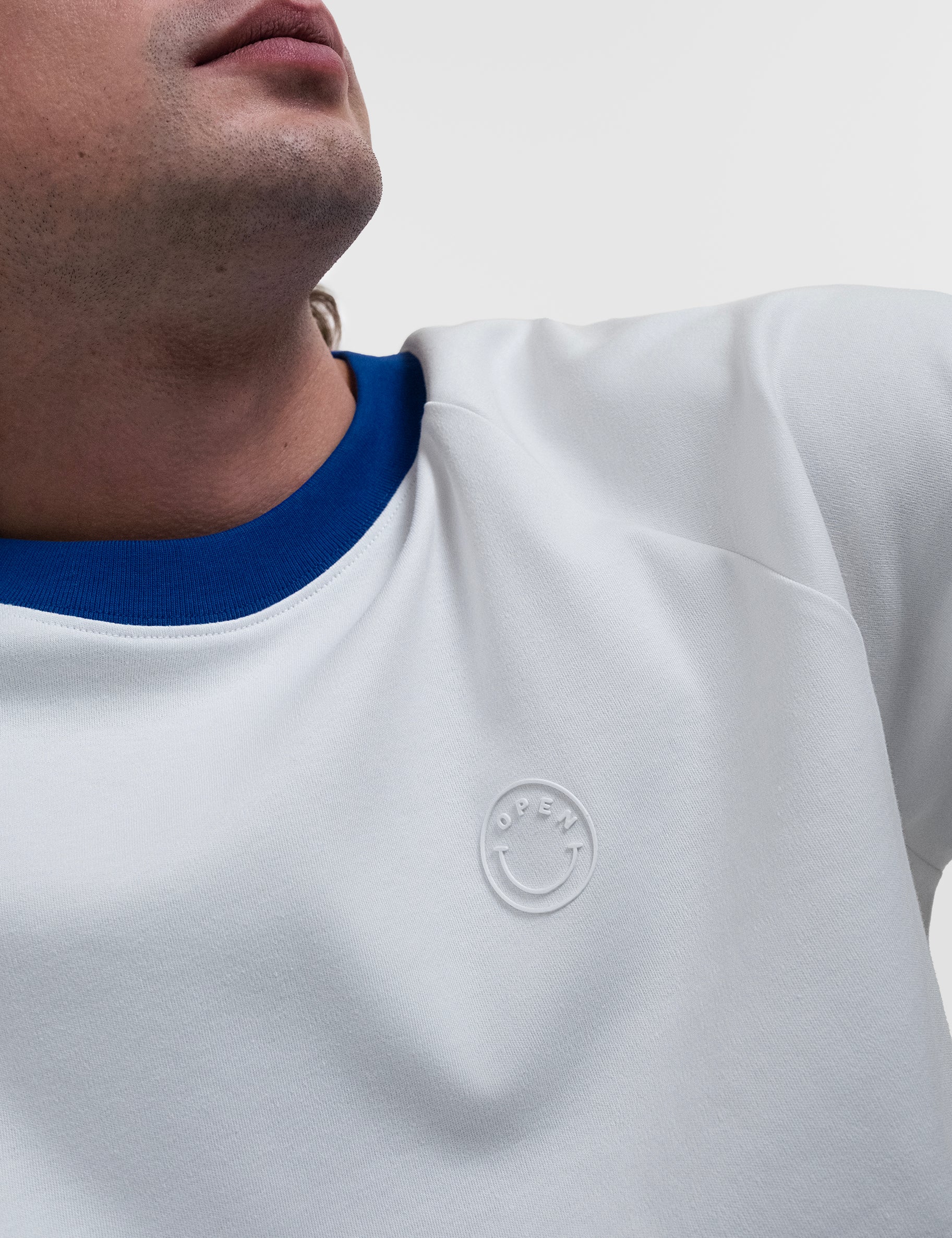 Open Row Men's Runaway Tee in white with blue collar, closeup view, embossed smiley logo detail.