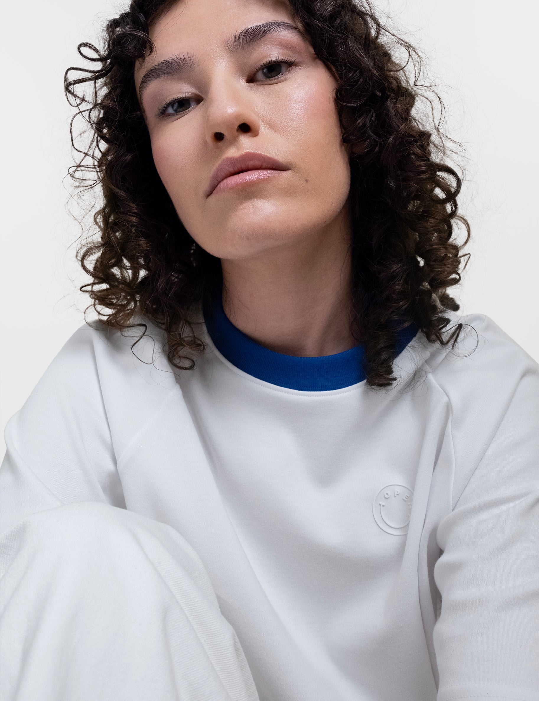 Open Row Women's Runaway Tee in white with blue collar, closeup view, embossed smiley logo detail.