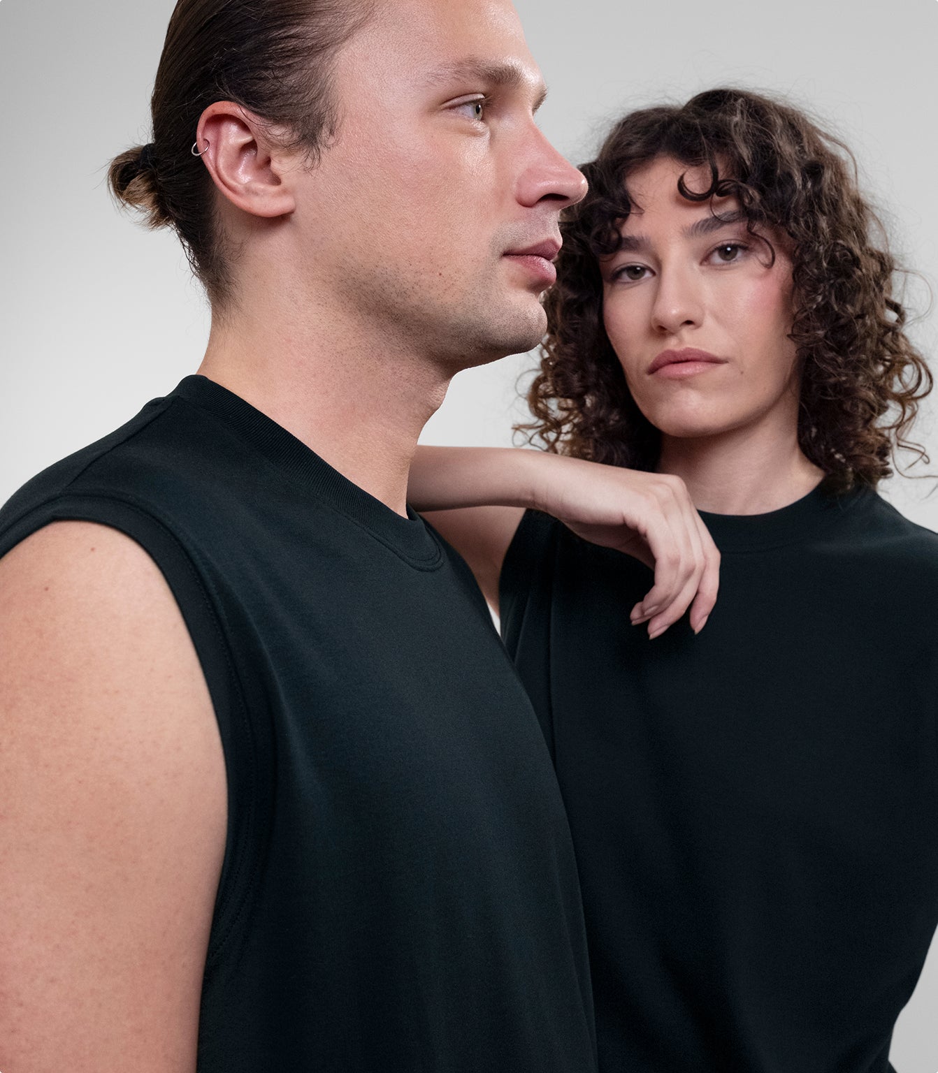 Two models wearing black Open Row Tank Tees, posed against a light gray studio background.