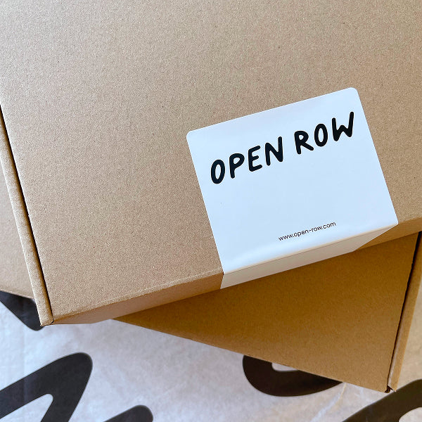 A close-up image of two cardboard boxes stacked together with a white sticker that shows the OPEN ROW logo and the website's URL.