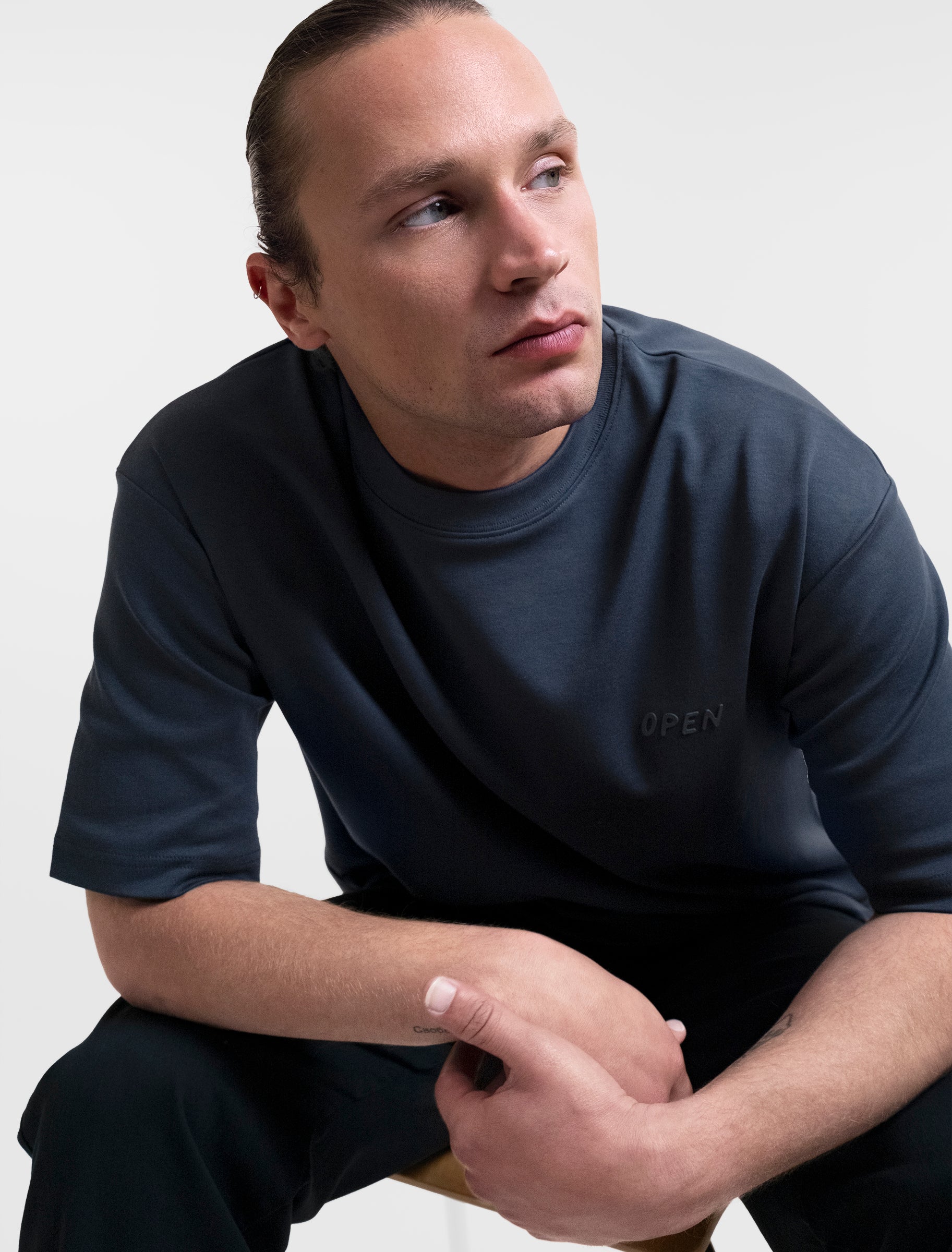 Open Row Men's Open Heart Tee in navy blue, front view sitting in a chair.