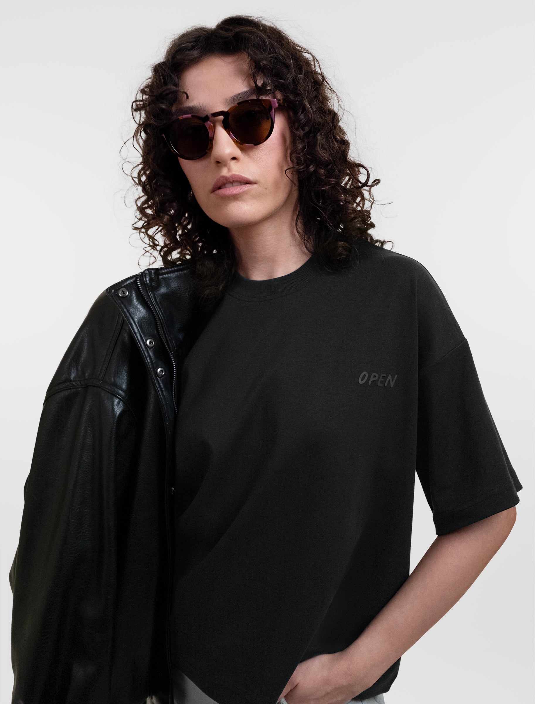 Open Row Women's Open Heart Tee in black, front editorial view paired with a leather jacket and sunglasses.