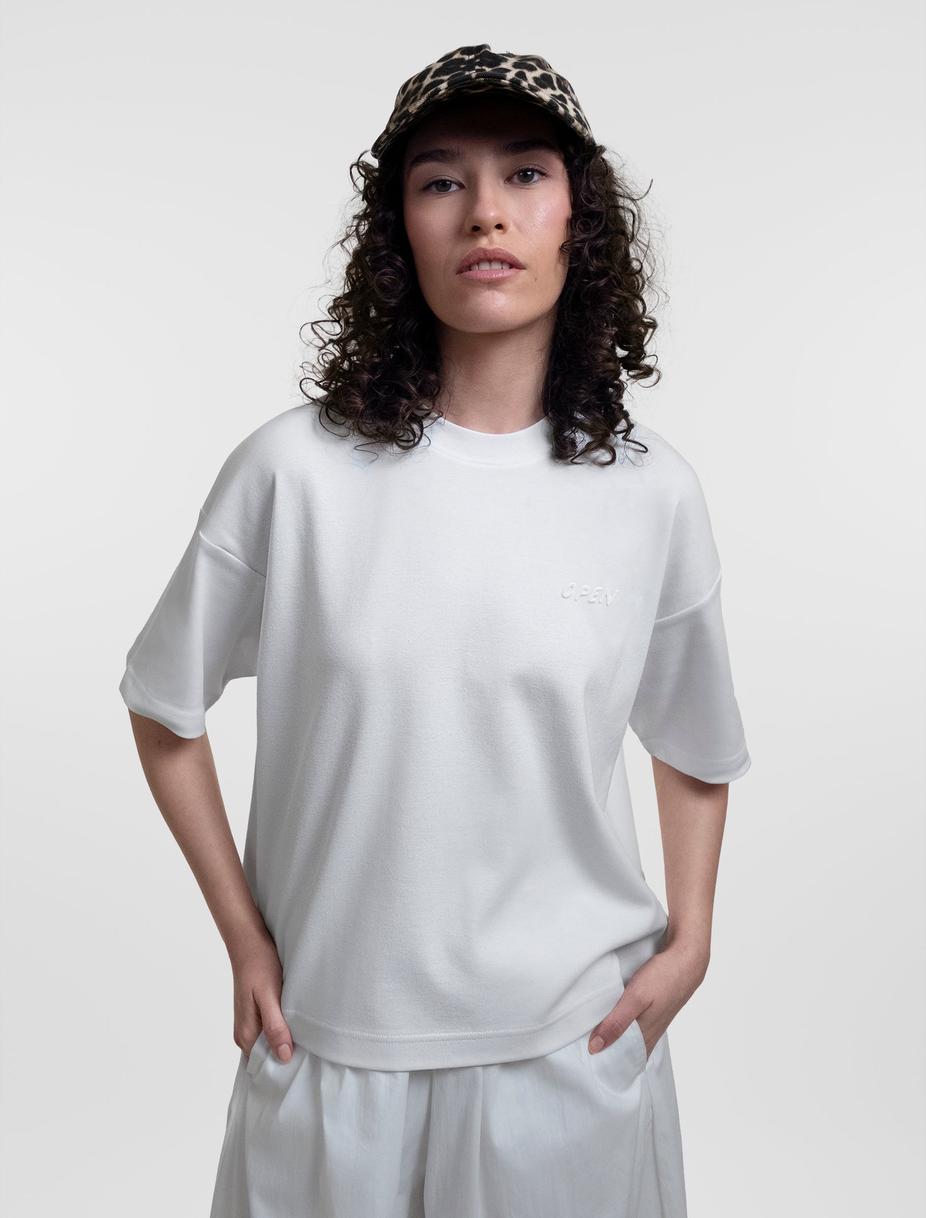 Open Row Women's Open Heart Tee in white, front view paired with a baseball cap.