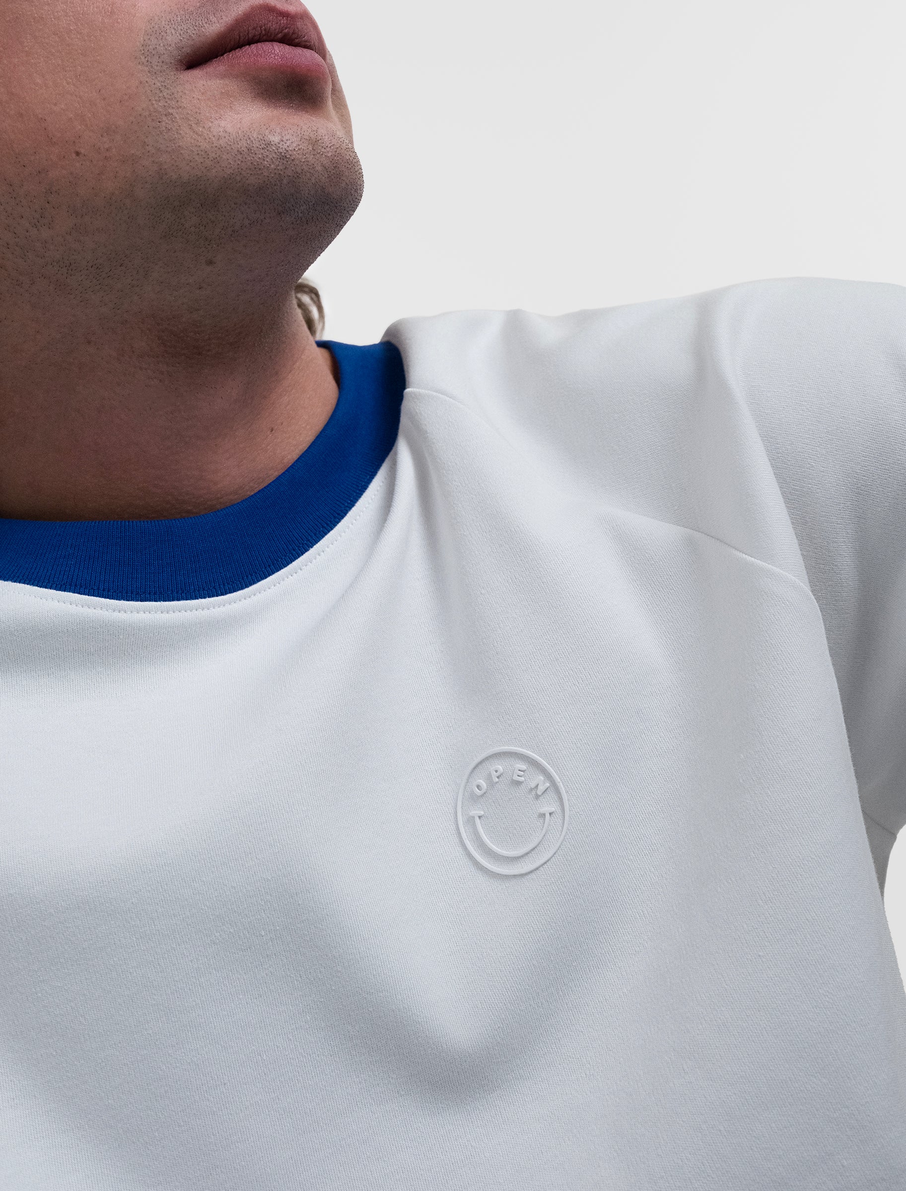 Open Row Men's Runaway Tee in white with blue collar, closeup view, embossed smiley logo detail.