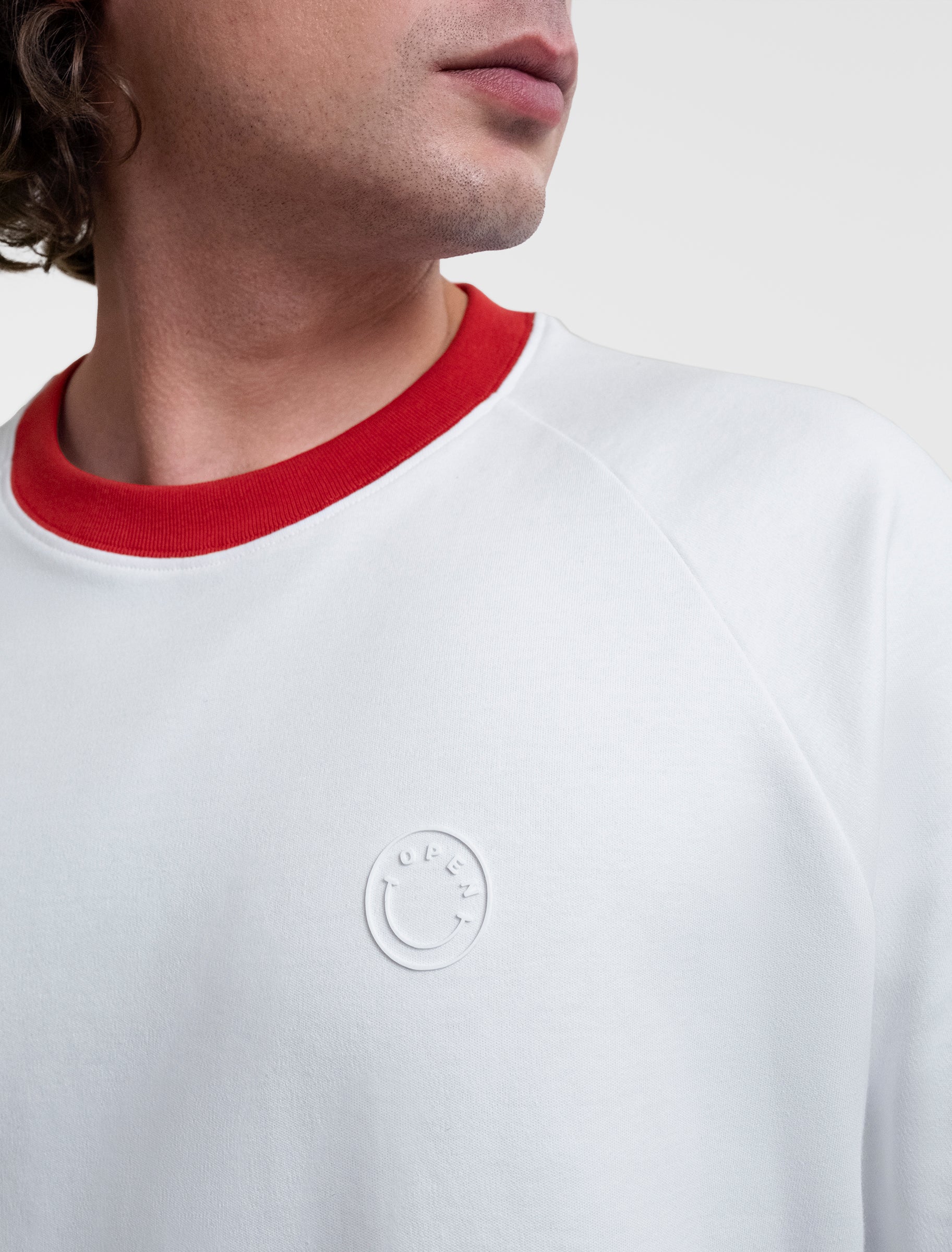 Open Row Men's Runaway Tee in white with red collar, closeup view, embossed smiley logo detail.
