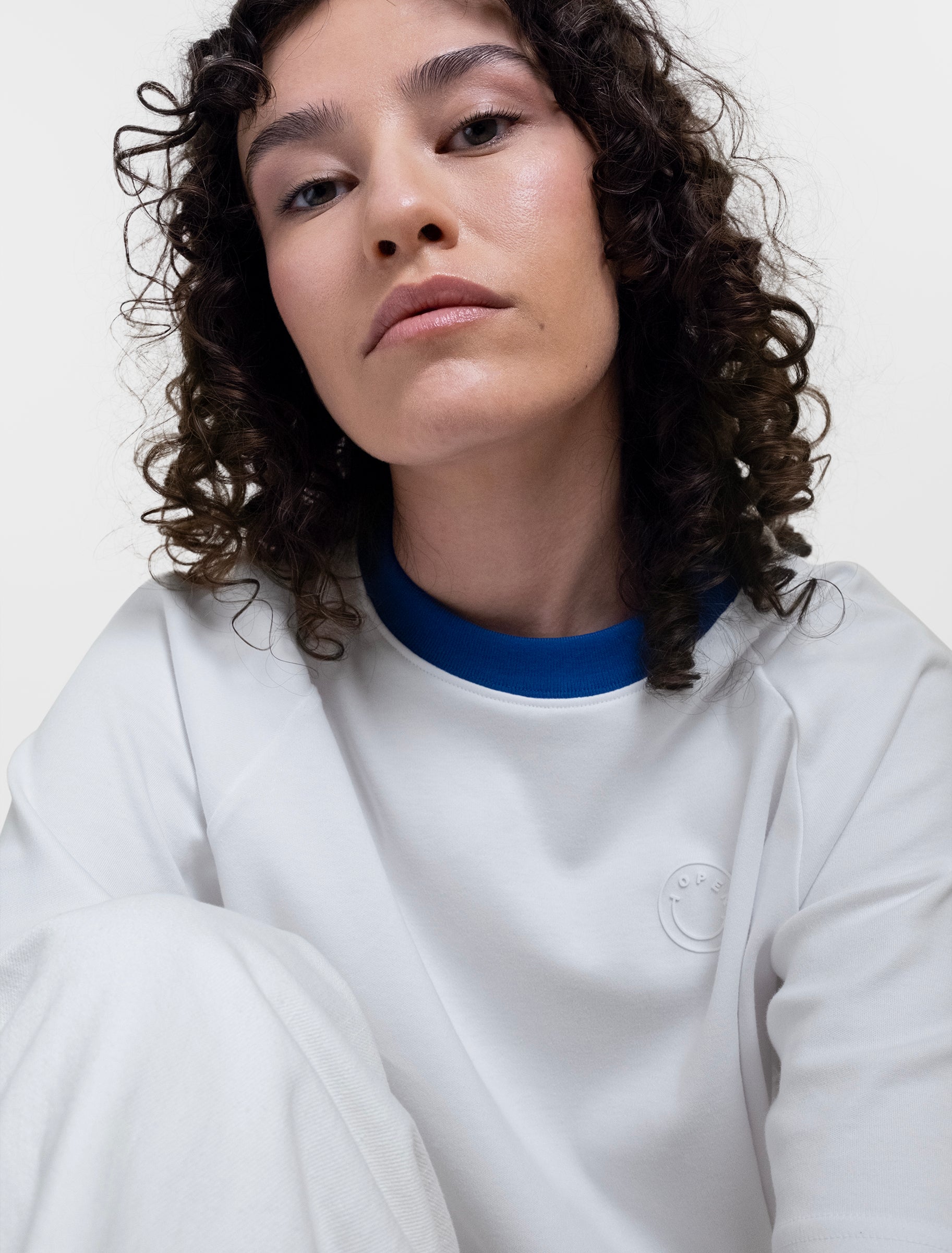 Open Row Women's Runaway Tee in white with blue collar, closeup view, embossed smiley logo detail.